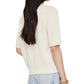 A woman with long dark hair wears the Anine Bing Jackson Sweater, a short-sleeve cream cashmere crewneck, paired with light blue jeans and a chunky gold bracelet, capturing effortless ANINE BING style from the back view.