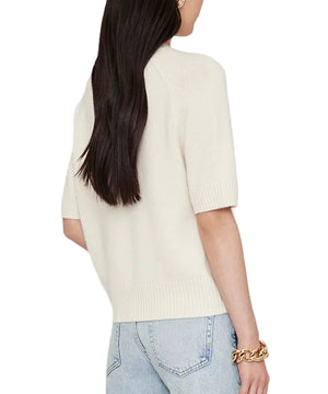 A woman with long dark hair wears the Anine Bing Jackson Sweater, a short-sleeve cream cashmere crewneck, paired with light blue jeans and a chunky gold bracelet, capturing effortless ANINE BING style from the back view.