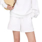 Wearing the Anine Bing Kam Short Framed Monogram sweatshirt and white shorts, a person holds a woven straw bag under their arm, hand in pocket, highlighting their outfit's midweight cotton comfort.