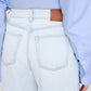 A person is shown from the back wearing Anine Bing's Manon Jean in an ultra-bleached blue wash with a brown leather patch and a light blue long-sleeve shirt.