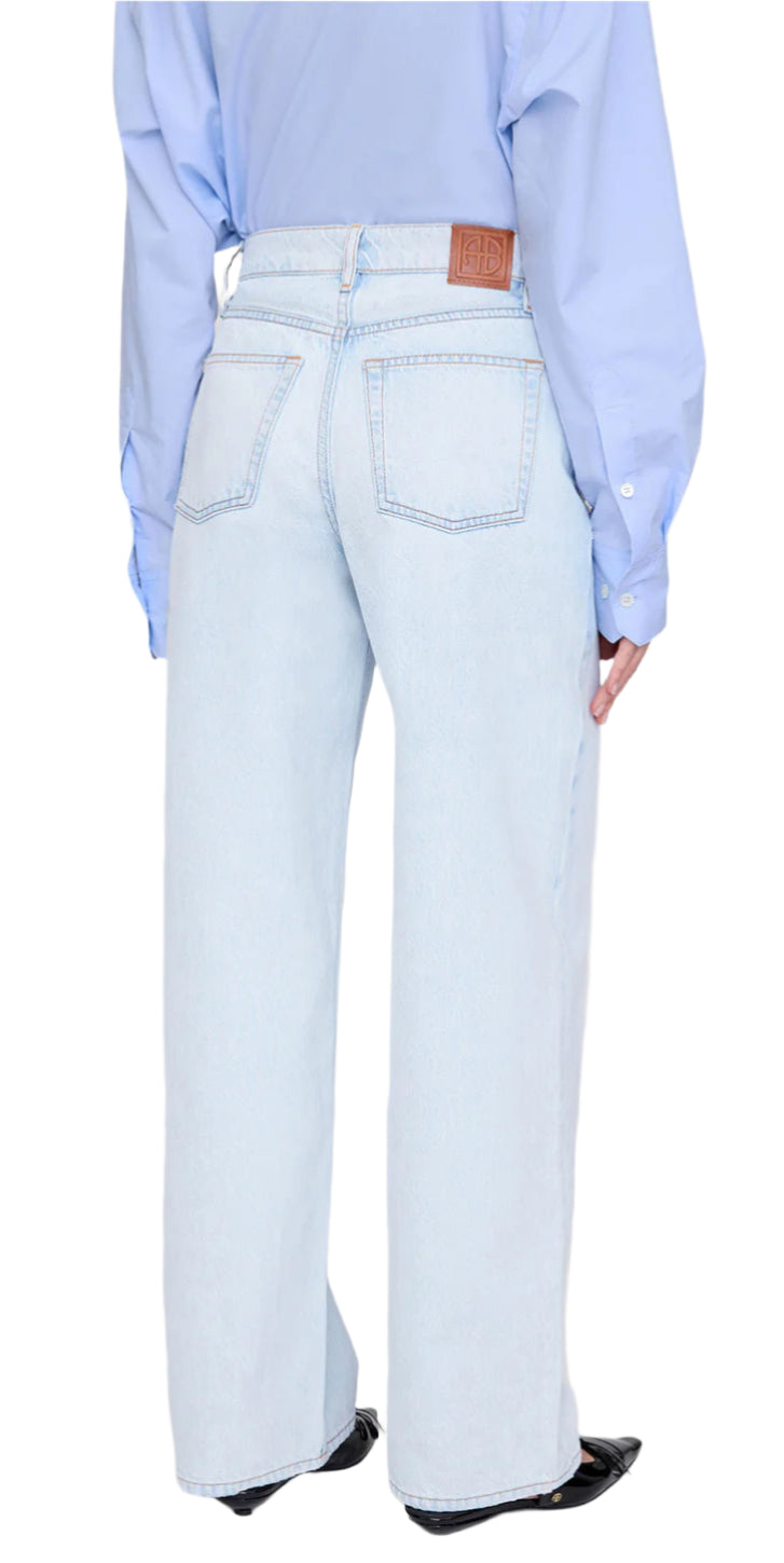 A person is seen from the back wearing Anine Bing’s Manon Jean in ultra-bleached blue with a baggy wide-leg fit, two back pockets, and a leather brand patch, paired with a light blue shirt.
