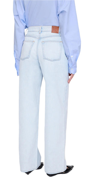 A person is seen from the back wearing Anine Bing’s Manon Jean in ultra-bleached blue with a baggy wide-leg fit, two back pockets, and a leather brand patch, paired with a light blue shirt.
