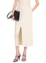 A woman styles the Anine Bing Meredith Skirt—a cream, high-rise tailored midi with a front slit—with black strappy heels and a matching black handbag. Her partially visible top adds to the skirt’s versatility, making it ideal for both office and after-hours looks.