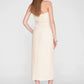 A woman stands facing away, wearing the Tyla Top by Anine Bing styled as a versatile beige strapless midi dress with a belt that accentuates her sculpted shape, paired with black high-heeled shoes against a plain light background.