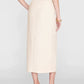 A woman stands facing away against a plain background, wearing the Anine Bing Meredith Skirt in beige—a high-rise waist midi skirt—paired with a matching top, black heeled sandals, and a gold bracelet.