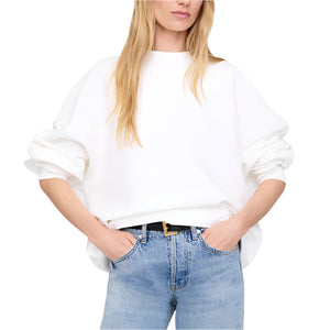A woman wears the Anine Bing Miles Sweatshirt Framed Monogram in white cotton fleece with long sleeves and pairs it with light blue jeans, standing with her hands in her front pockets.