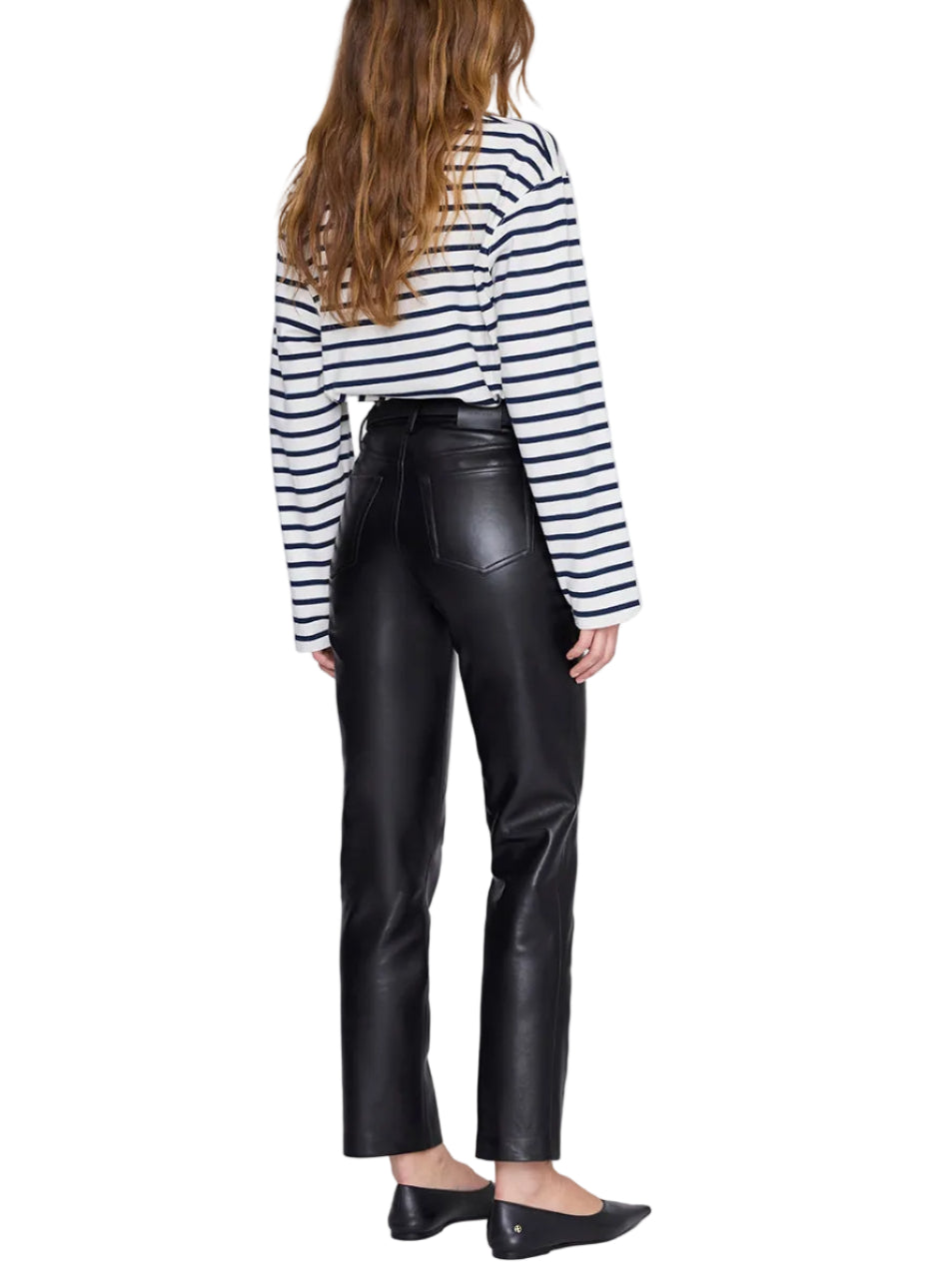 A person stands with their back to the camera, wearing the Anine Bing Newton Tee—a navy striped long sleeve with a boat neckline—paired with black leather pants and black flats.