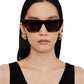 A woman with straight dark hair wears Anine Bing Paris Sunglasses—cat-eye tortoise acetate frames with polarized lenses—plus gold hoop earrings and a sleeveless black top against a plain background.