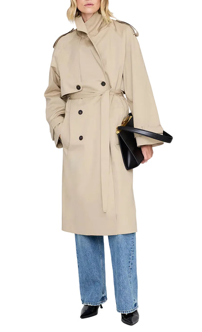 A person wearing the Anine Bing Rickie Maxi Trench, light blue jeans, black shoes, and holding a black handbag stands against a plain background.