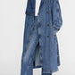 A woman wears the Rickie Maxi Denim Trench by Anine Bing over matching denim pants, a white top, and pointed black shoes for a chic, menswear-inspired look.