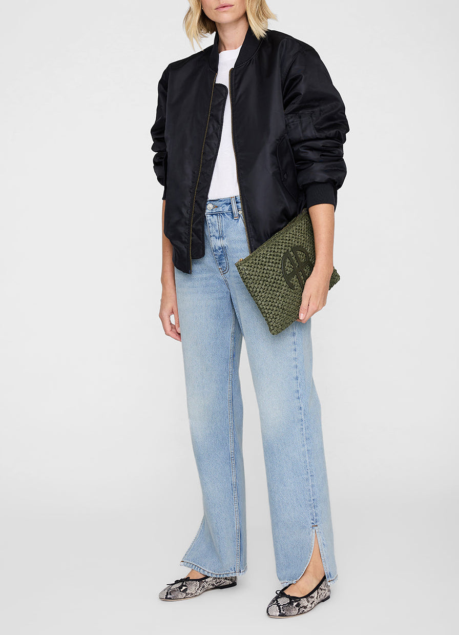 A woman wears a black bomber jacket, white t-shirt, light blue front-slit jeans, snakeskin flats, and carries the Anine Bing Rio Woven Pouch.