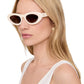 A woman with long blonde hair wears Anine Bing Roma Sunglasses—bone acetate oval frames with brown gradient lenses—and a white tank top, facing left against a plain white background.
