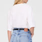 A person with long blonde hair is seen from behind, wearing a relaxed white Rudy Tee by Anine Bing and light blue high-waisted jeans featuring a brown patch on the waistband.