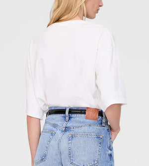 A person with long blonde hair is seen from behind, wearing a relaxed white Rudy Tee by Anine Bing and light blue high-waisted jeans featuring a brown patch on the waistband.