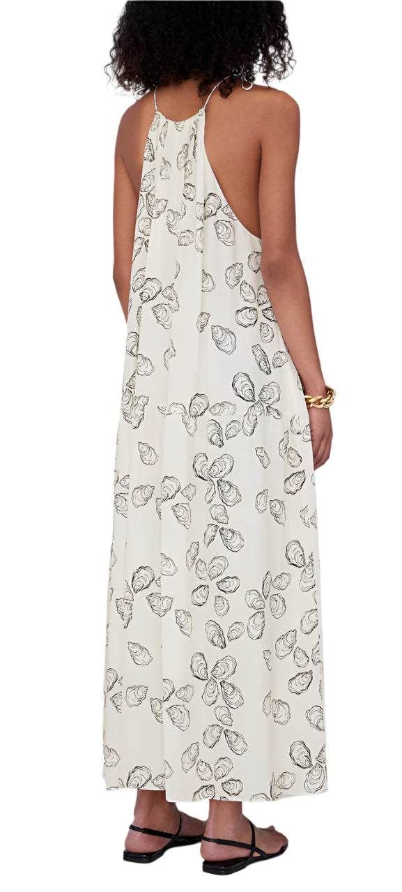 A woman in a Santana Dress by Anine Bing, featuring a long floral pattern and crafted from a luxurious viscose-silk blend, exuding elegance. She is seen from the back wearing sandals and a bracelet.