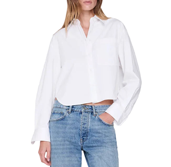 A woman wearing the Anine Bing Scott Cropped Shirt—a white, long-sleeve cotton poplin button-down with front pockets—paired with blue jeans, stands against a plain white background.