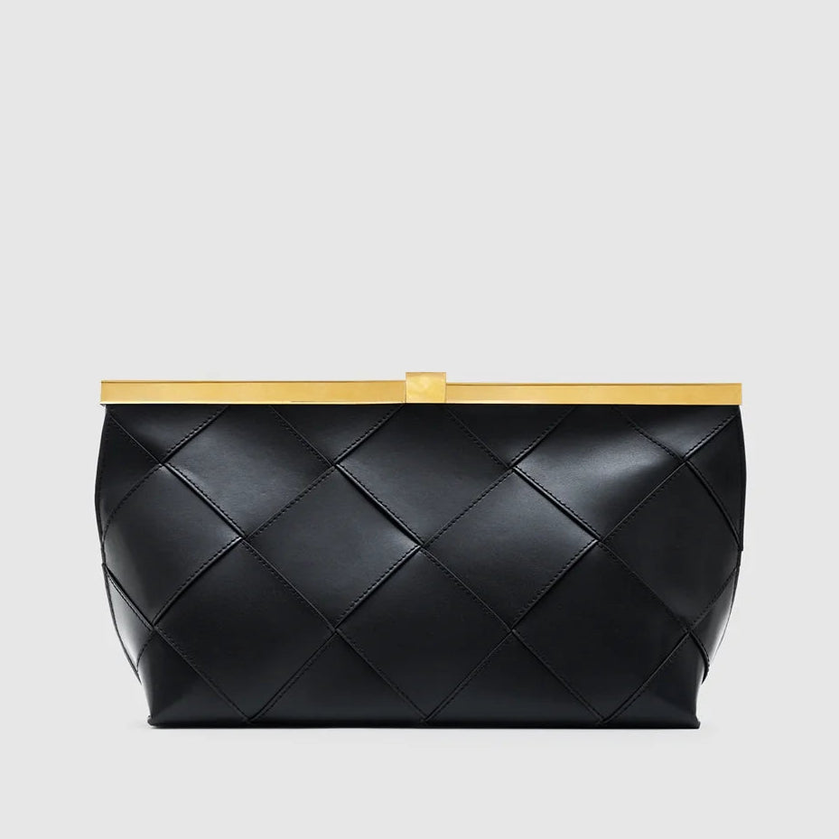 The Anine Bing Anine Braided Leather Clutch features black leather with a bold braided pattern and is topped with a rectangular gold metal frame, creating a sculptural silhouette that makes it a true statement piece, shown against a plain light background.