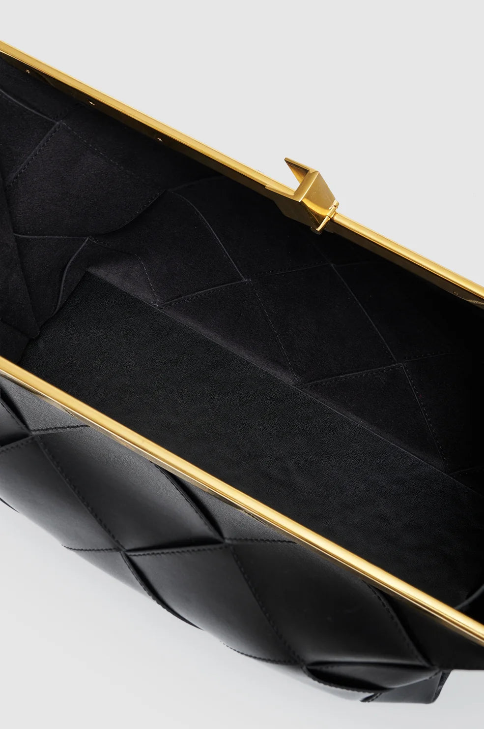 Close-up view of an open Anine Bing Anine Braided Leather Clutch, featuring a black braided leather exterior with a gold metal frame and clasp, showcasing its empty black fabric interior.