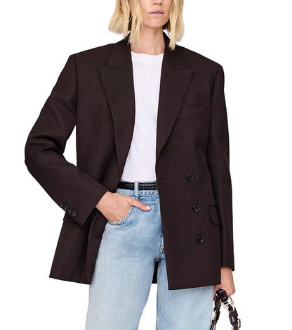 A woman wears the Aretha Blazer by Anine Bing—a slim hourglass-fit tuxedo wool blazer with a notched collar—over a white t-shirt and light blue jeans, with one hand in her pocket and the other holding a small bag.