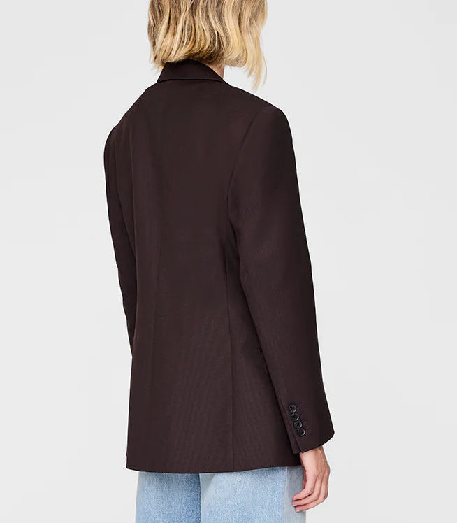 A person is shown from the back against a plain light background, wearing the Anine Bing Aretha Blazer—a black wool tuxedo jacket with a notched collar and slim hourglass fit—paired with light blue jeans.