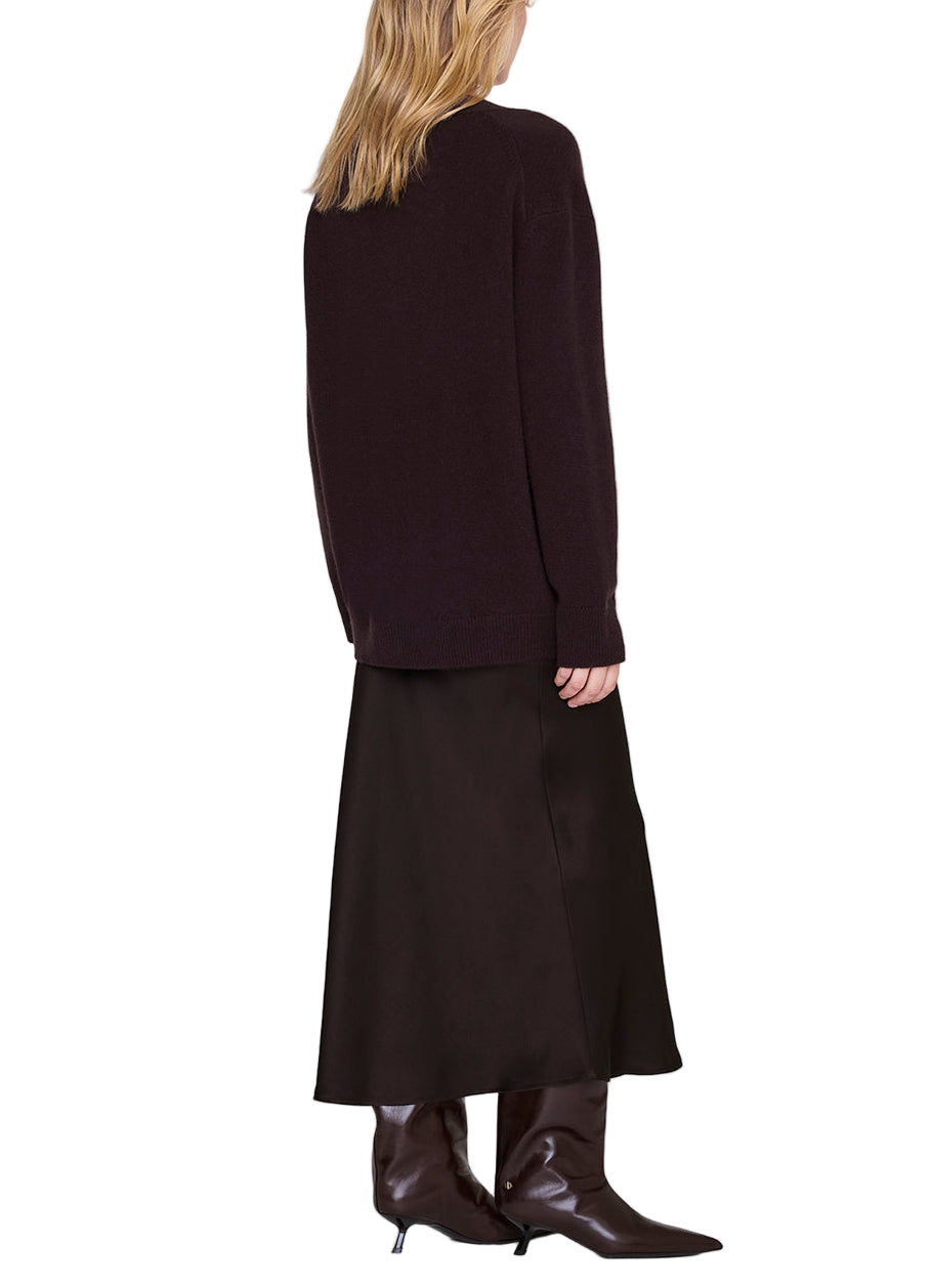 A person stands with their back to the camera, wearing a dark sweater, brown heeled boots, and an Anine Bing Bar Silk Skirt in black.