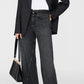 A person wearing a black blazer, white T-shirt, Anine Bing Brie Jeans in a dark wash relaxed silhouette, black heeled boots, and holding a black handbag.