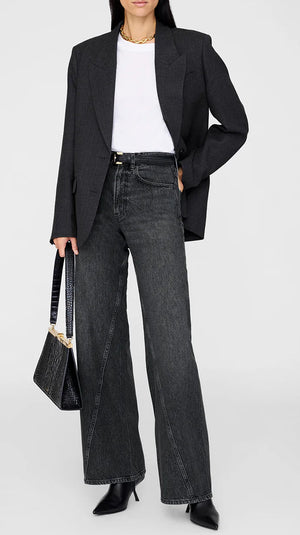 A person wearing a black blazer, white T-shirt, Anine Bing Brie Jeans in a dark wash relaxed silhouette, black heeled boots, and holding a black handbag.