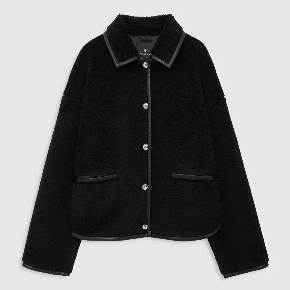 The Camden Jacket by Anine Bing is a black textured wool blend workwear style featuring button closure, two front pockets, and leather-like trim accents on the collar, pockets, cuffs, and hem. It is displayed against a plain light background.