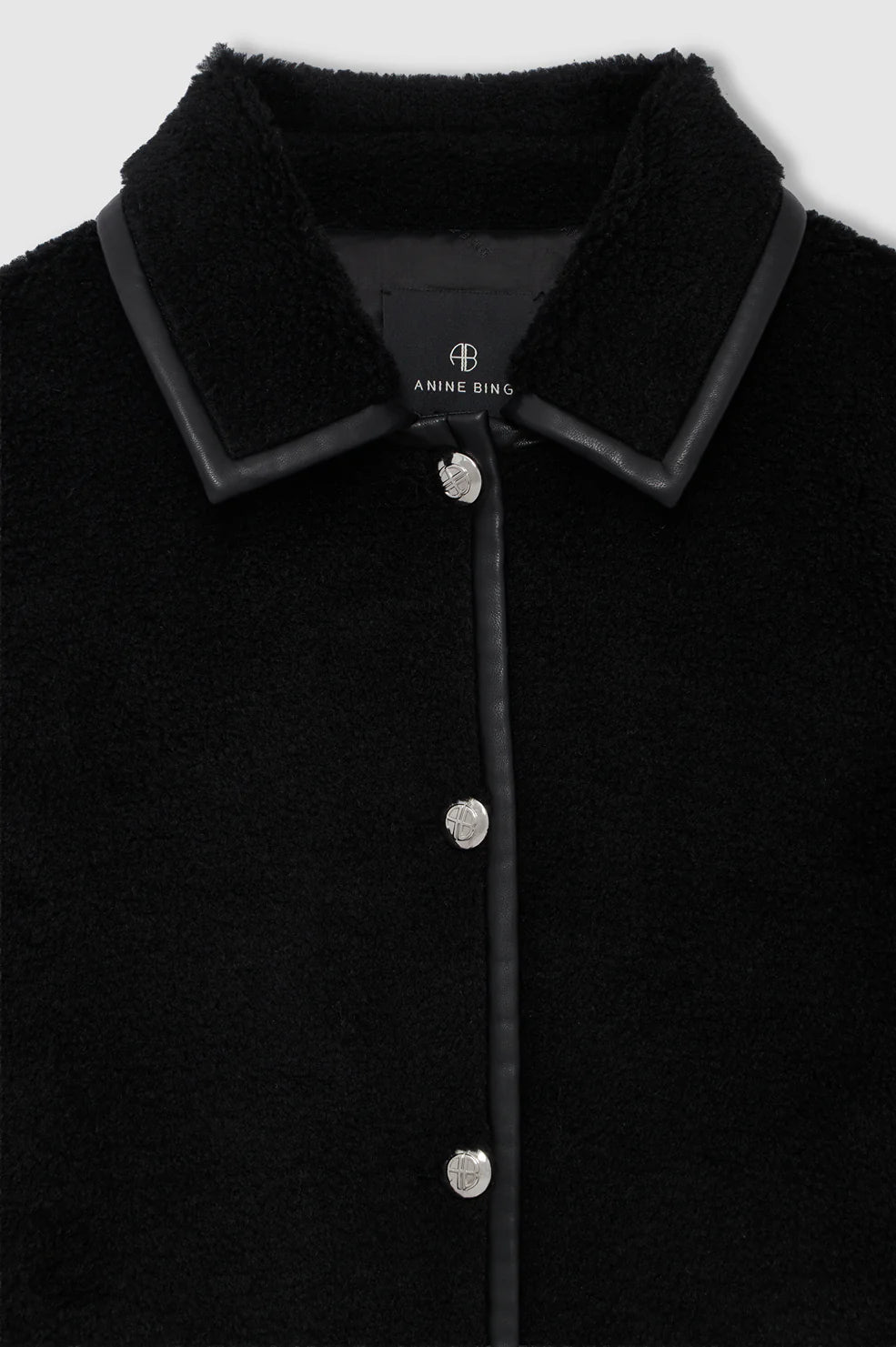 Close-up of the Anine Bing Camden Jacket, featuring a black textured wool blend fabric, a black leather-trimmed collar, and silver buttons, with an “Anine Bing” label displayed inside the collar.