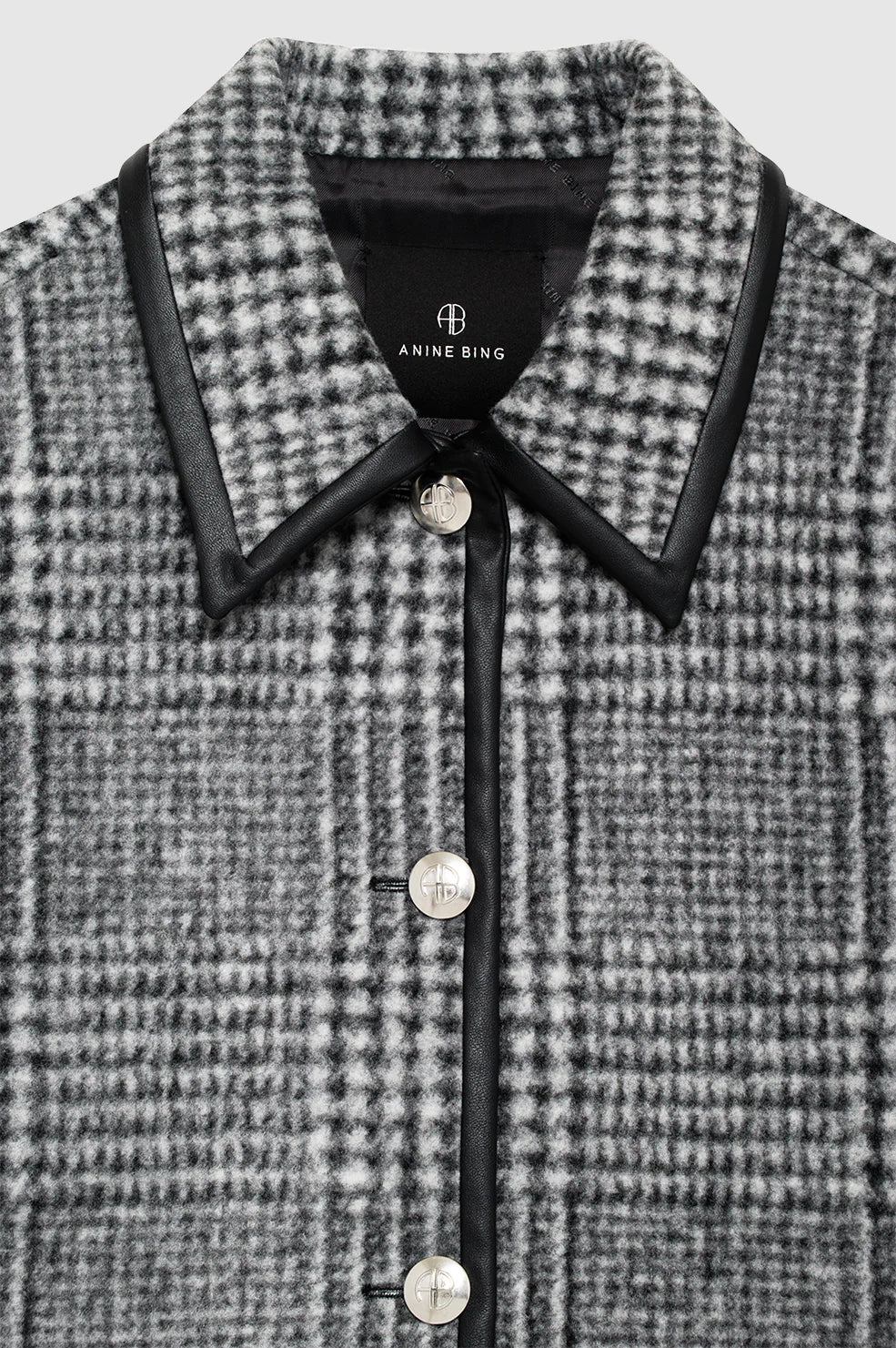 Close-up of the Camden Jacket by Anine Bing: a gray and black houndstooth-patterned wool blend coat with a pointed collar, black trim, and silver buttons.