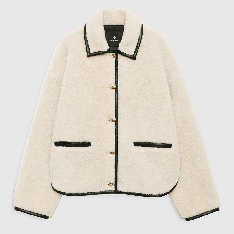 The Camden Jacket by Anine Bing is a cream button-up wool-blend sherpa workwear jacket, featuring black trim on the collar, hem, cuffs, buttons, and pockets, shown laid flat on a plain background.