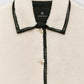 Close-up of the Anine Bing Camden Jacket, a cream-colored wool blend shearling workwear style with black leather trim, collar, and buttons, featuring the brand label inside the collar.