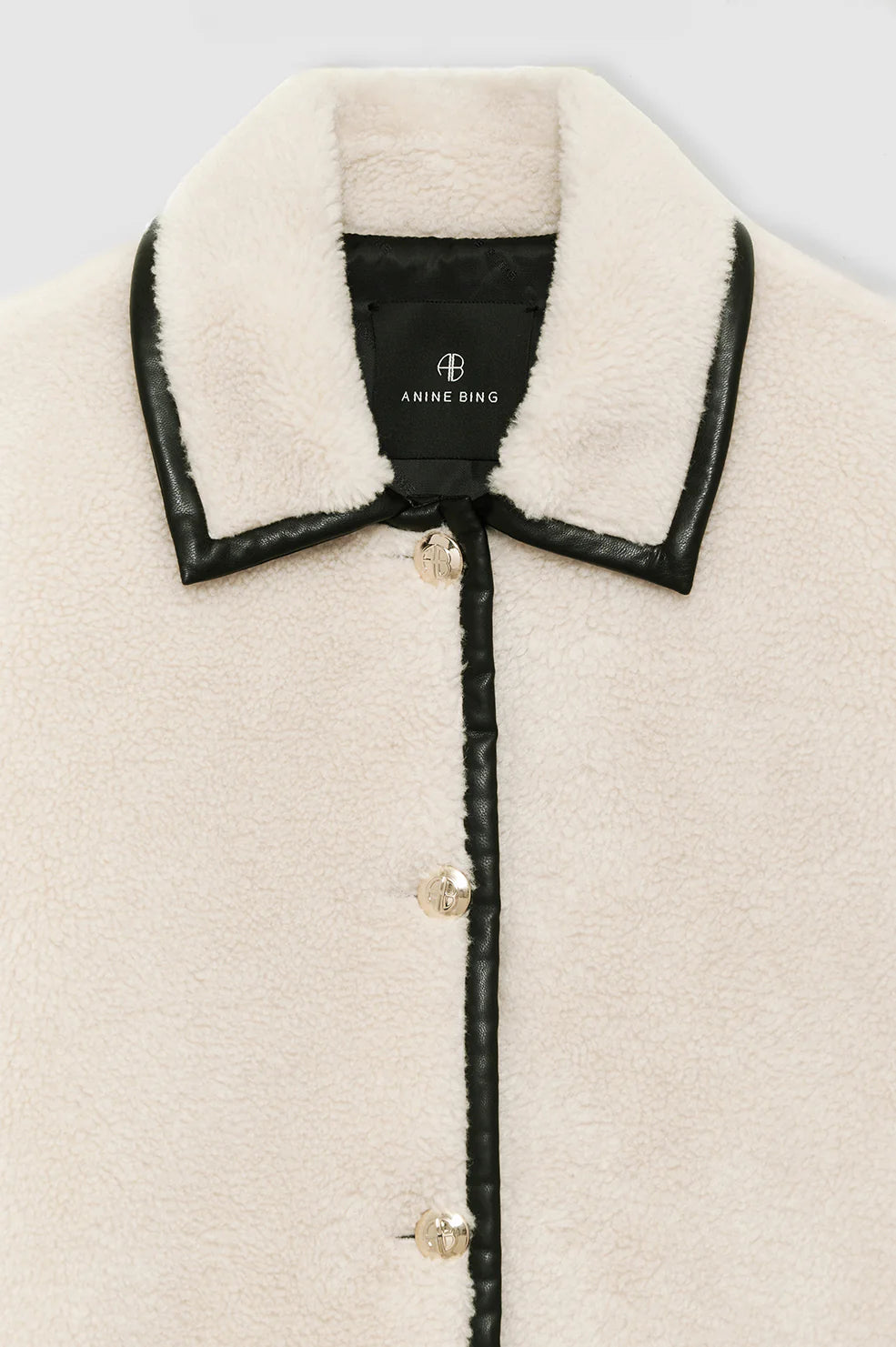 Close-up of the Anine Bing Camden Jacket, a cream-colored wool blend shearling workwear style with black leather trim, collar, and buttons, featuring the brand label inside the collar.