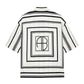 The Coco Shirt Monogram Stripe by Anine Bing is a boxy, short-sleeve white button-up with black geometric square patterns and "AB" letters inside a central square on the back, made from a lightweight cupro blend for comfort.