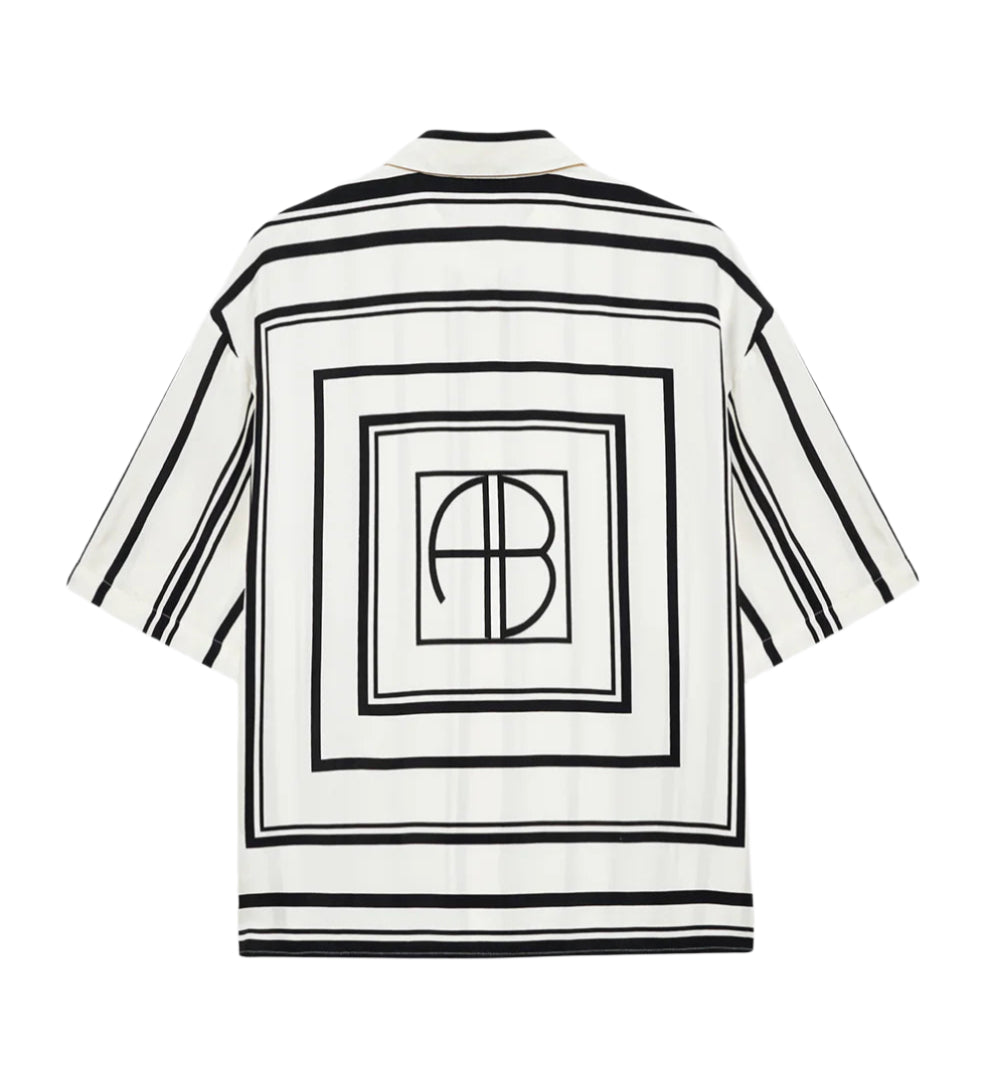 The Coco Shirt Monogram Stripe by Anine Bing is a boxy, short-sleeve white button-up with black geometric square patterns and "AB" letters inside a central square on the back, made from a lightweight cupro blend for comfort.