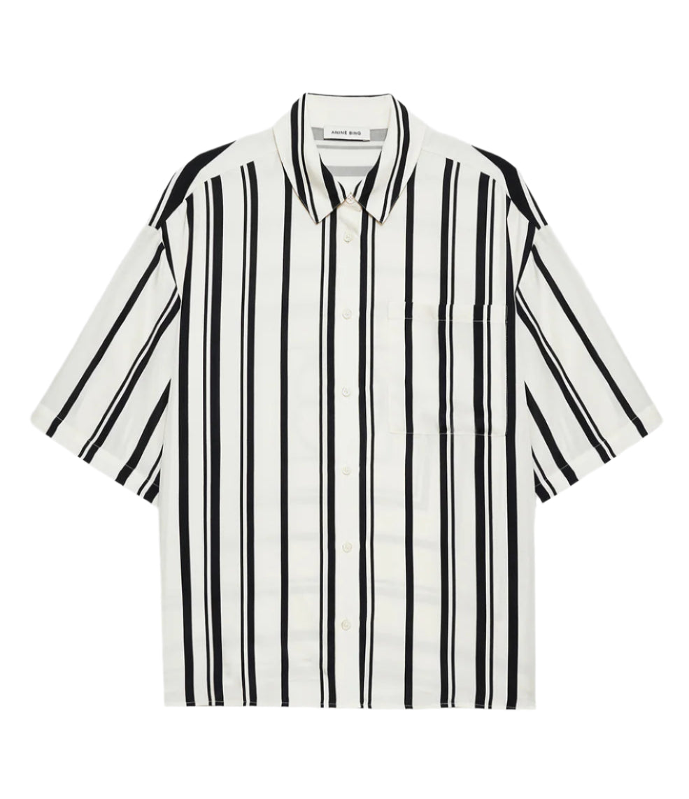 The Anine Bing Coco Shirt Monogram Stripe is a boxy collared shirt in a lightweight cupro blend with ivory and black vertical stripes, short sleeves, and a chest pocket, shown laid flat on a white background.