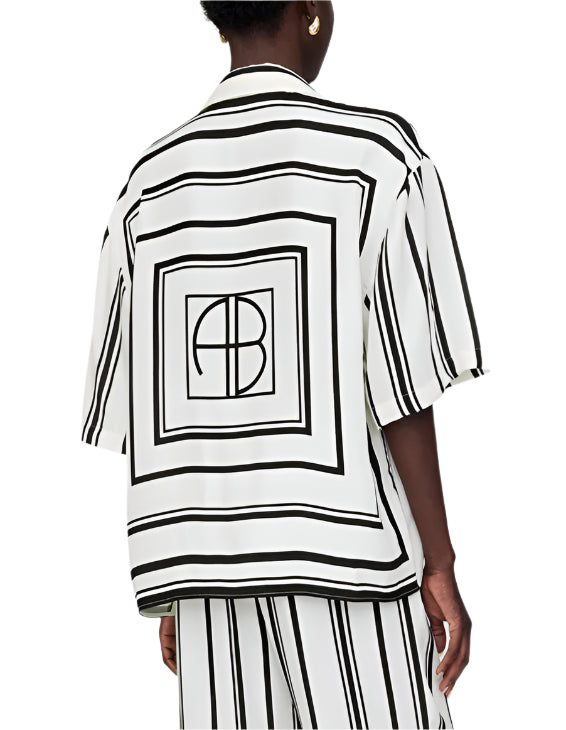 Person wears the Anine Bing Coco Shirt Monogram Stripe, featuring an ivory and black geometric stripe pattern with "AB" lettering on the back, paired with matching striped cupro-blend pants.