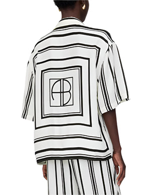 Person wears the Anine Bing Coco Shirt Monogram Stripe, featuring an ivory and black geometric stripe pattern with "AB" lettering on the back, paired with matching striped cupro-blend pants.