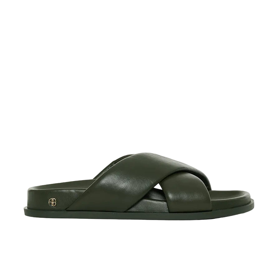 The Emi Slides by Anine Bing are dark green flat sandals featuring wide, overlapping crisscross padded lambskin leather straps and a flat sole, shown in a side profile view.