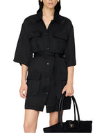 A woman wearing the Anine Bing Geri Dress—a washed black cupro dress with a waist tie and large front pockets—holds a black woven tote bag.