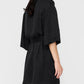 A woman stands sideways wearing the Anine Bing Geri Dress, a loose-fitting washed black cupro dress featuring short sleeves and a belted waist.