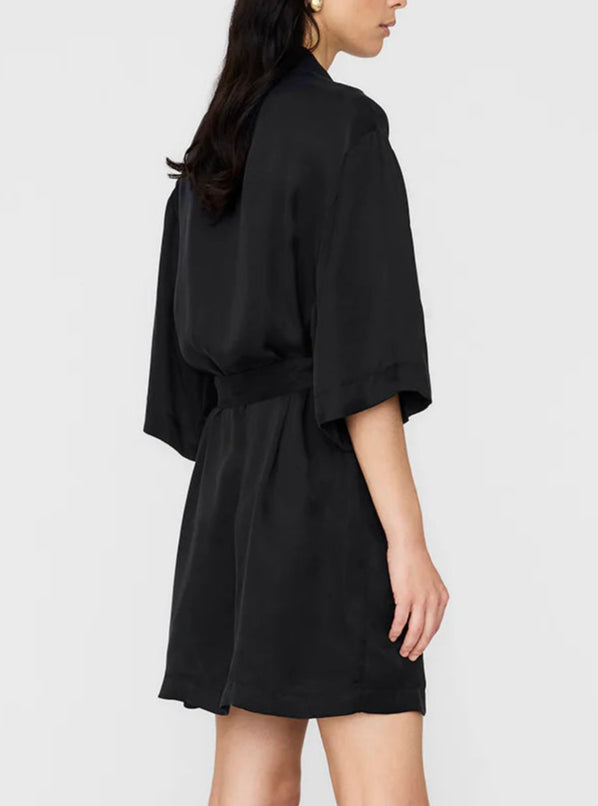 A woman stands sideways wearing the Anine Bing Geri Dress, a loose-fitting washed black cupro dress featuring short sleeves and a belted waist.
