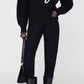 A person in an Anine Bing Kendrick Sweater Bing, black pants, patent boots, and a black handbag stands against a plain background, embodying modern AB branding style.