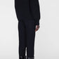 Person standing against a plain background, wearing a black Kendrick Sweater Bing by Anine Bing, black pants, and black patent knee-high heeled boots—an elevated look with a subtle nod to AB branding.