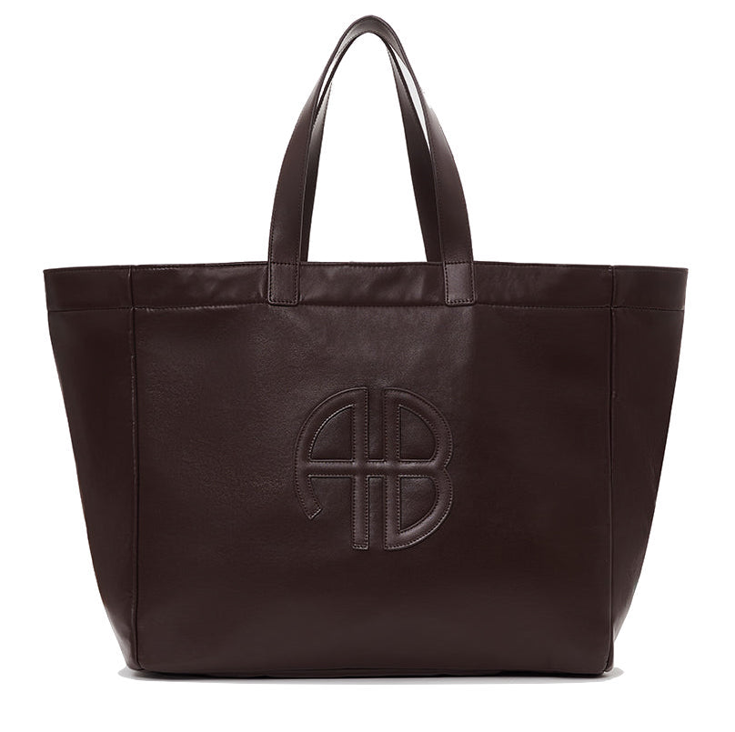 The Large Rio Tote by Anine Bing is a spacious dark brown leather bag with two handles and an embossed circular AB logo on the front—an essential for everyday use.