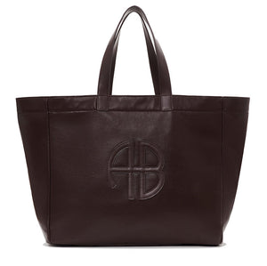 The Large Rio Tote by Anine Bing is a spacious dark brown leather bag with two handles and an embossed circular AB logo on the front—an essential for everyday use.