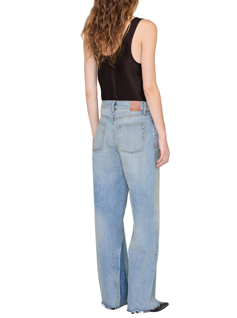 A person with long wavy hair, seen from behind, wears the Anine Bing Lea Top in black silk charmeuse paired with light blue high-waisted wide-leg jeans for a relaxed silhouette.