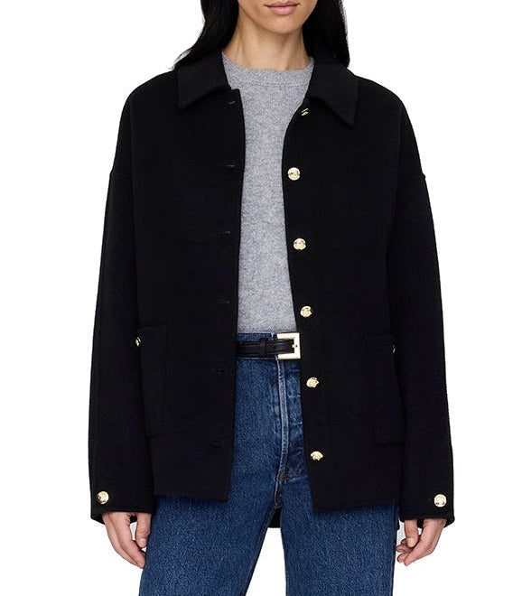 A woman wears the Anine Bing Luca Cashmere Blend Jacket in black over a gray shirt and blue jeans, standing with her hands by her sides.
