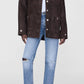 A person in the Anine Bing Luca Suede Jacket—a dark brown button-up—paired with a white shirt, ripped light blue jeans, and pointed dark brown ankle boots stands against a plain background.