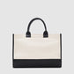 The Anine Bing Medium Lara Tote features a cream cotton canvas body with black leather trim and handles, shown against a simple light background.